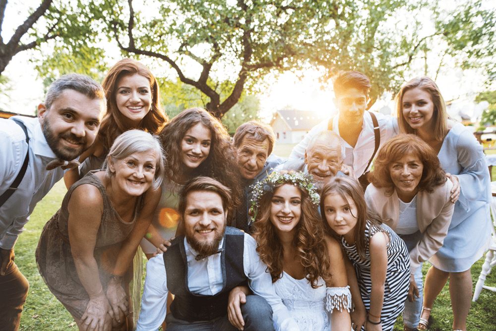 A joyful group of family and friends poses together outdoors, celebrating a wedding.