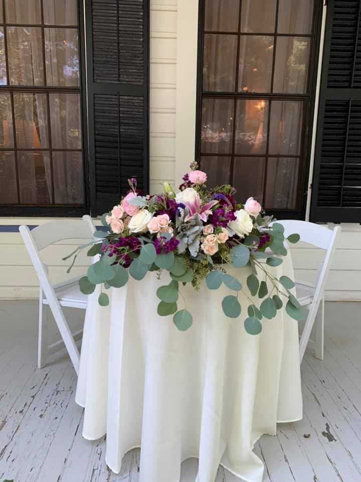 A elegantly arranged floral centerpiece with roses and greenery on a table by a window.