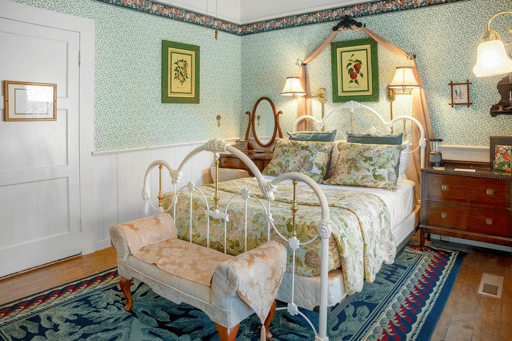 Cozy bedroom featuring a white metal bed, floral bedding, and vintage decor with green walls.